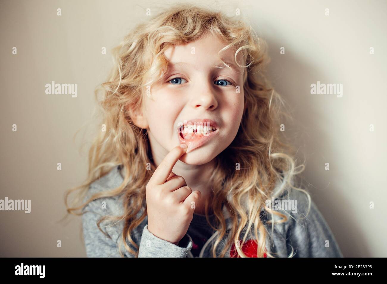 Cute caucasica bionda ragazza mostrando il suo dente mancante in bocca. Bambino orgoglioso che mostra il dente perso e si aspetta una fata dente che dà i suoi soldi. Ringhino Foto Stock