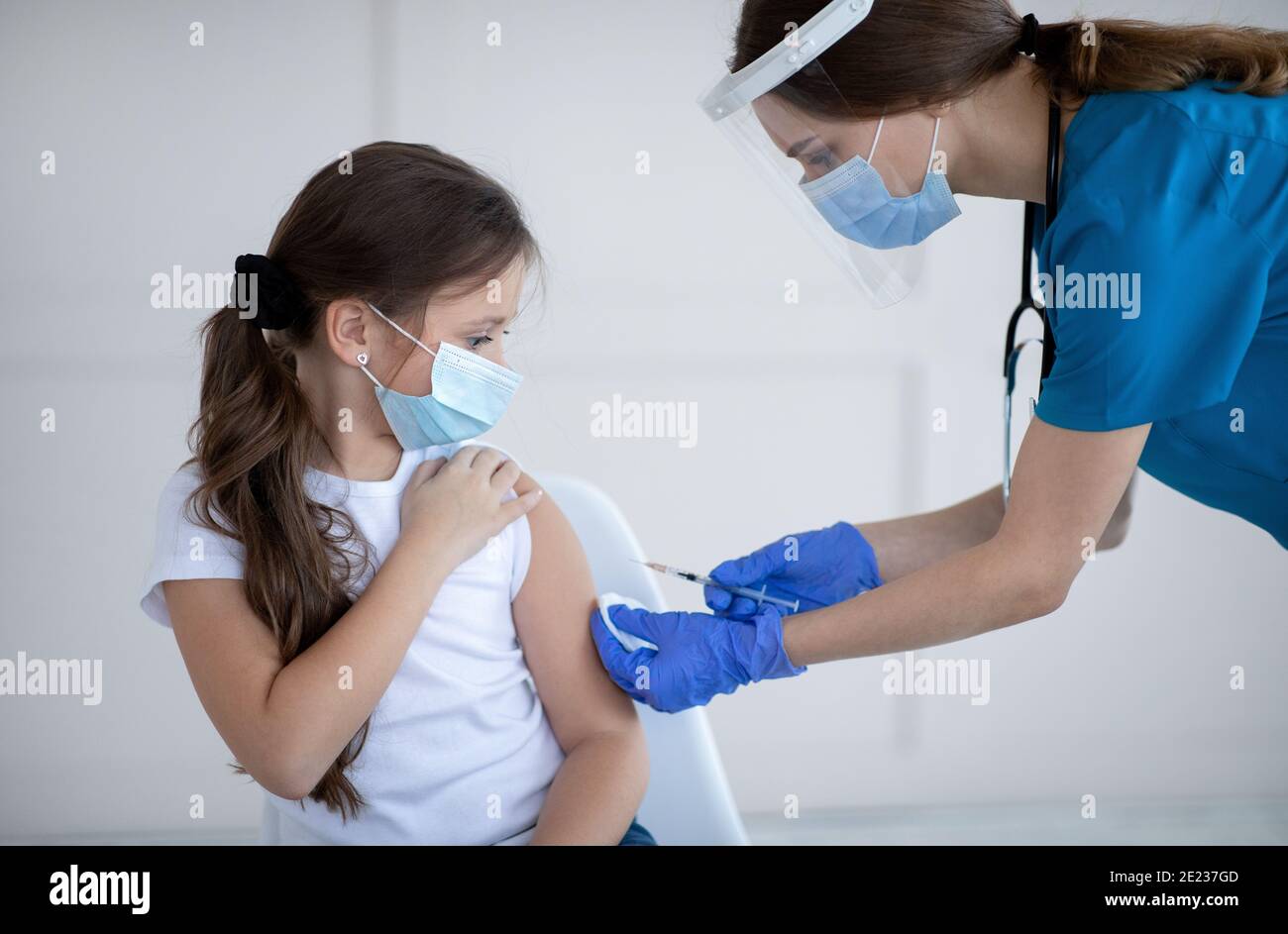 Vaccinazione di Covid-19. Bambina in maschera protettiva che riceve l'iniezione del vaccino del coronavirus dal medico presso la clinica Foto Stock