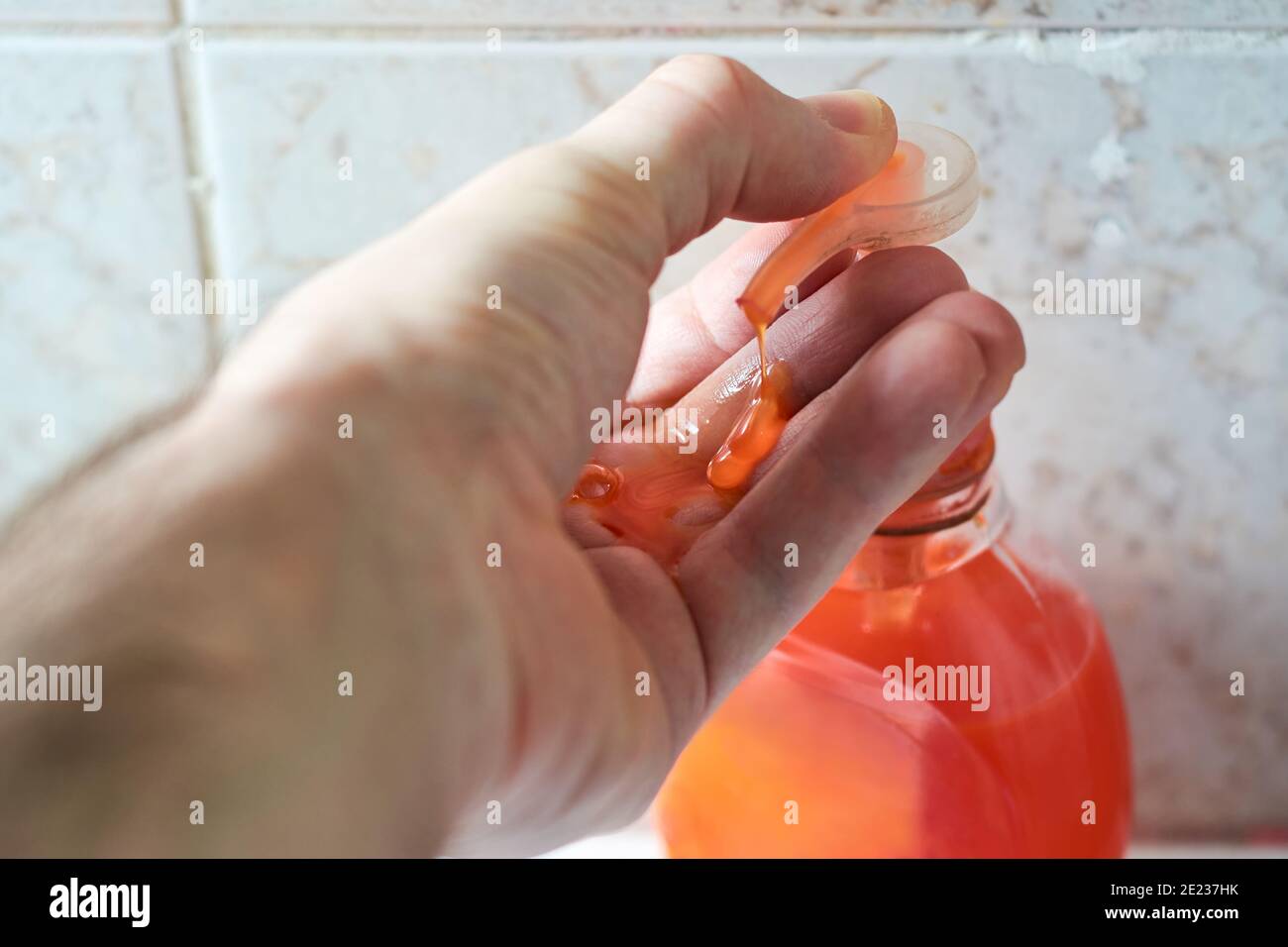 Chiusura della mano maschio con sapone liquido, pressione della pompa dell'erogatore con il pollice e applicazione del flusso di sapone sul palmo. Concetto di igiene personale. Foto Stock