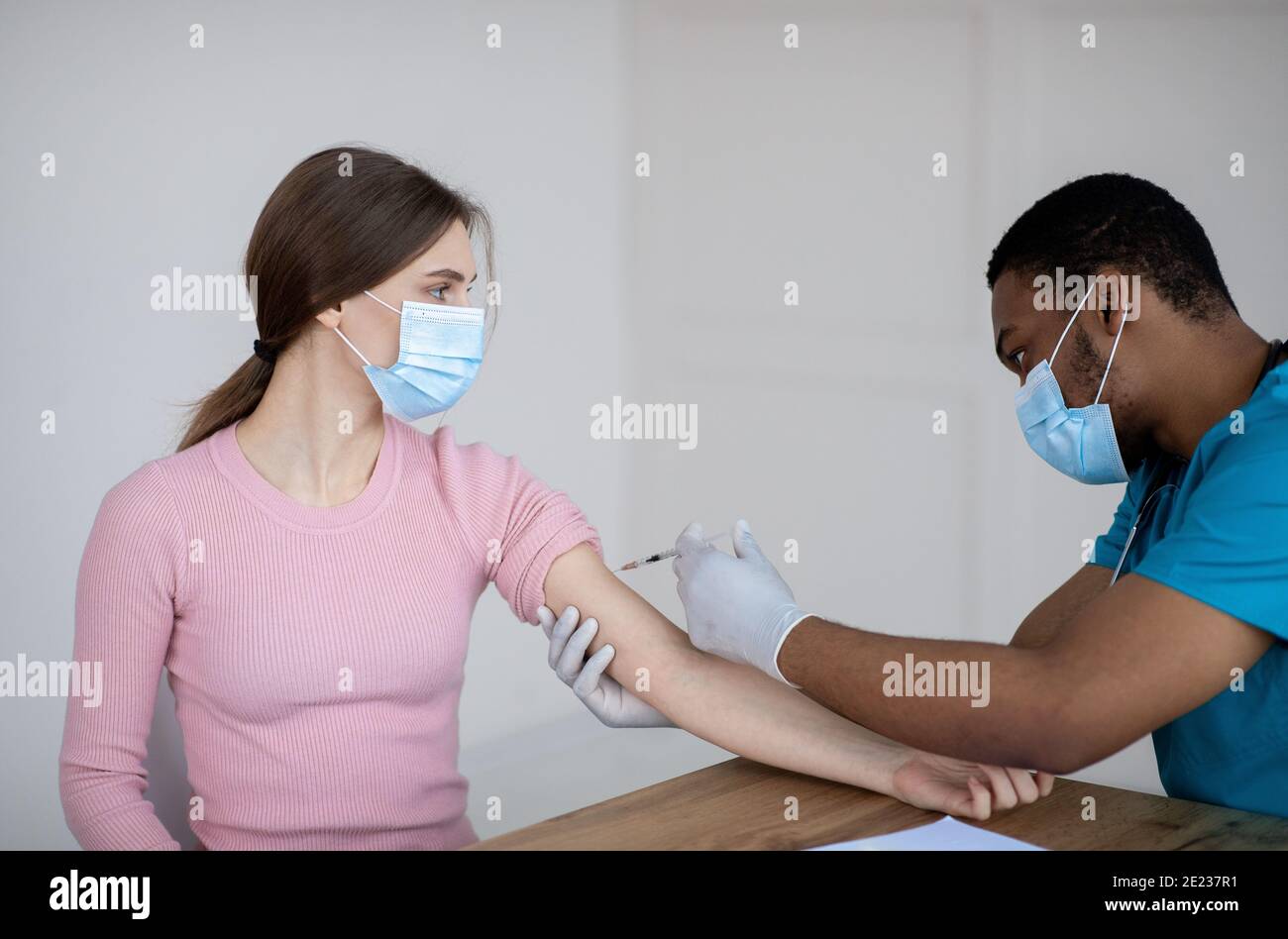 Medico nero che fa l'iniezione del vaccino di covid-19 alla paziente femminile in clinica. Cure mediche contro la pandemia globale Foto Stock
