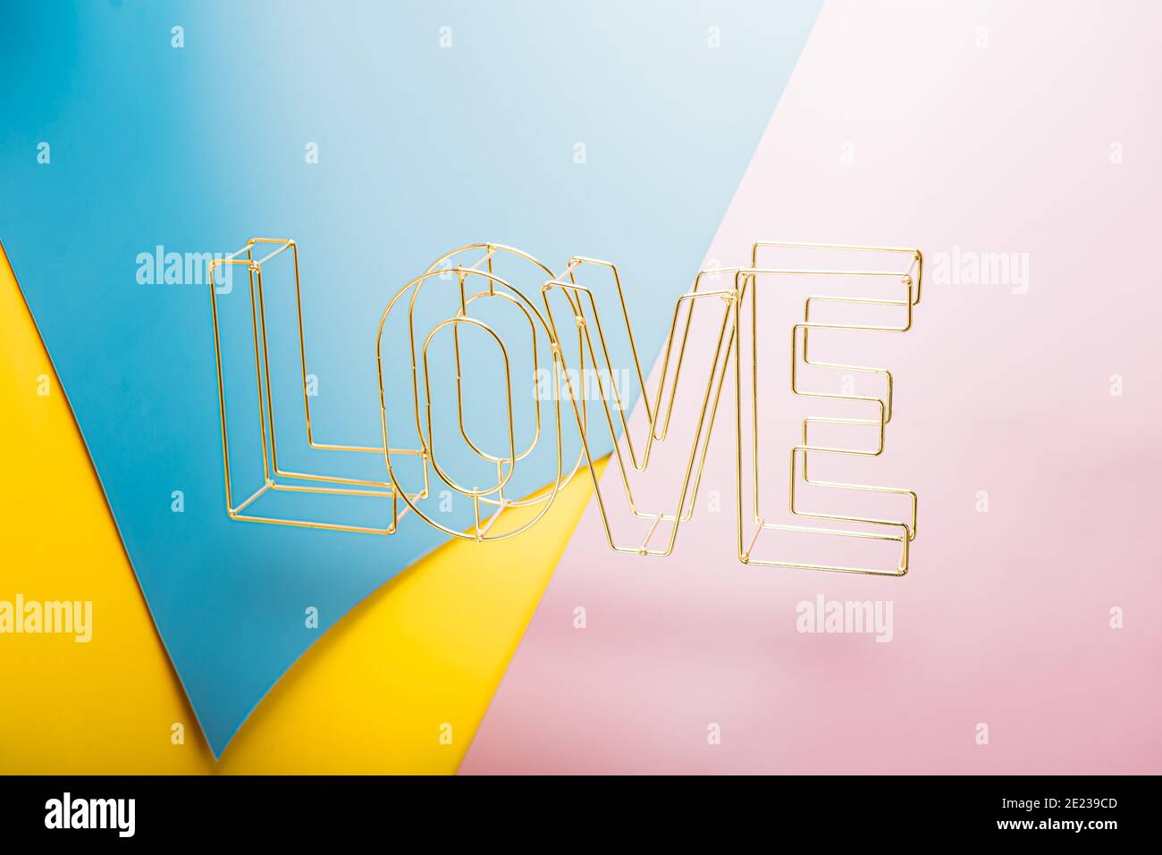 Golden 3d Wire Love word che si leva su sfondo misto blu, rosa e giallo. Carta creativa di San Valentino. Concetto di amore. Spazio di copia Foto Stock