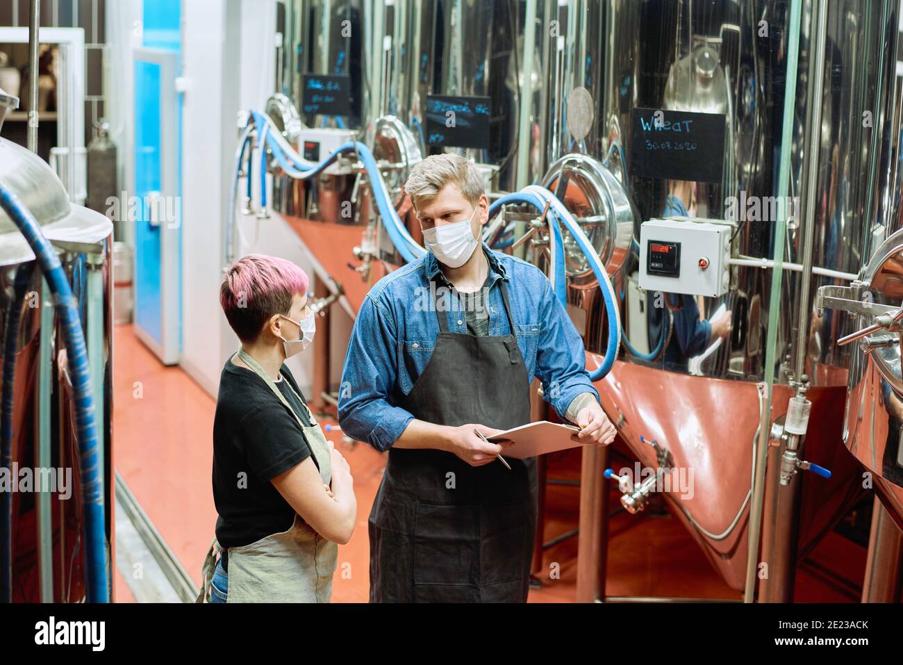 Due giovani produttori di grandi birrifici contemporanei di consulenza per la produzione di birra circa alcuni momenti di lavoro tra serbatoi di acciaio Foto Stock