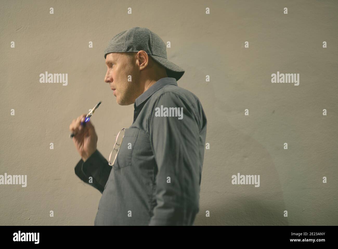 Uomo maturo fumare sigaretta elettronica contro parete grigia di cemento Foto Stock
