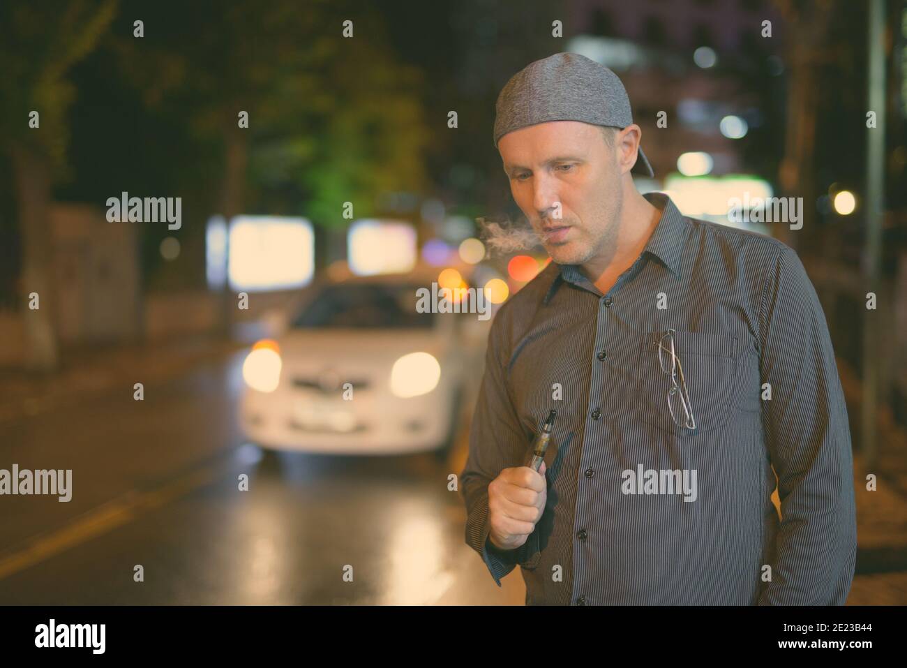 Uomo maturo di fumare sigarette elettroniche per le strade di notte Foto Stock