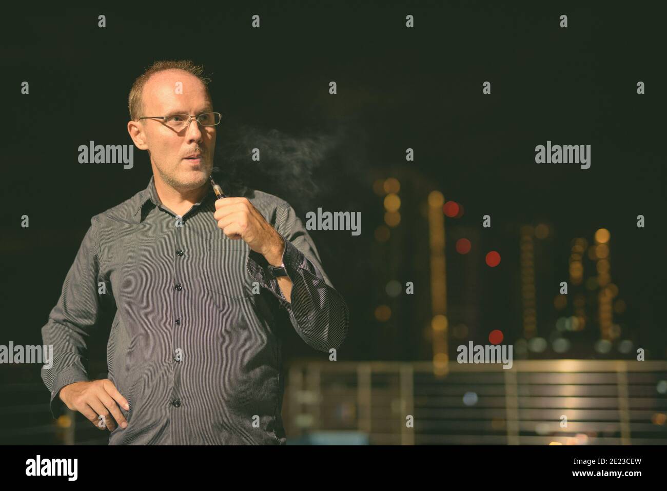 Uomo maturo che fuma sigaretta elettronica sulla piscina sul tetto Foto Stock