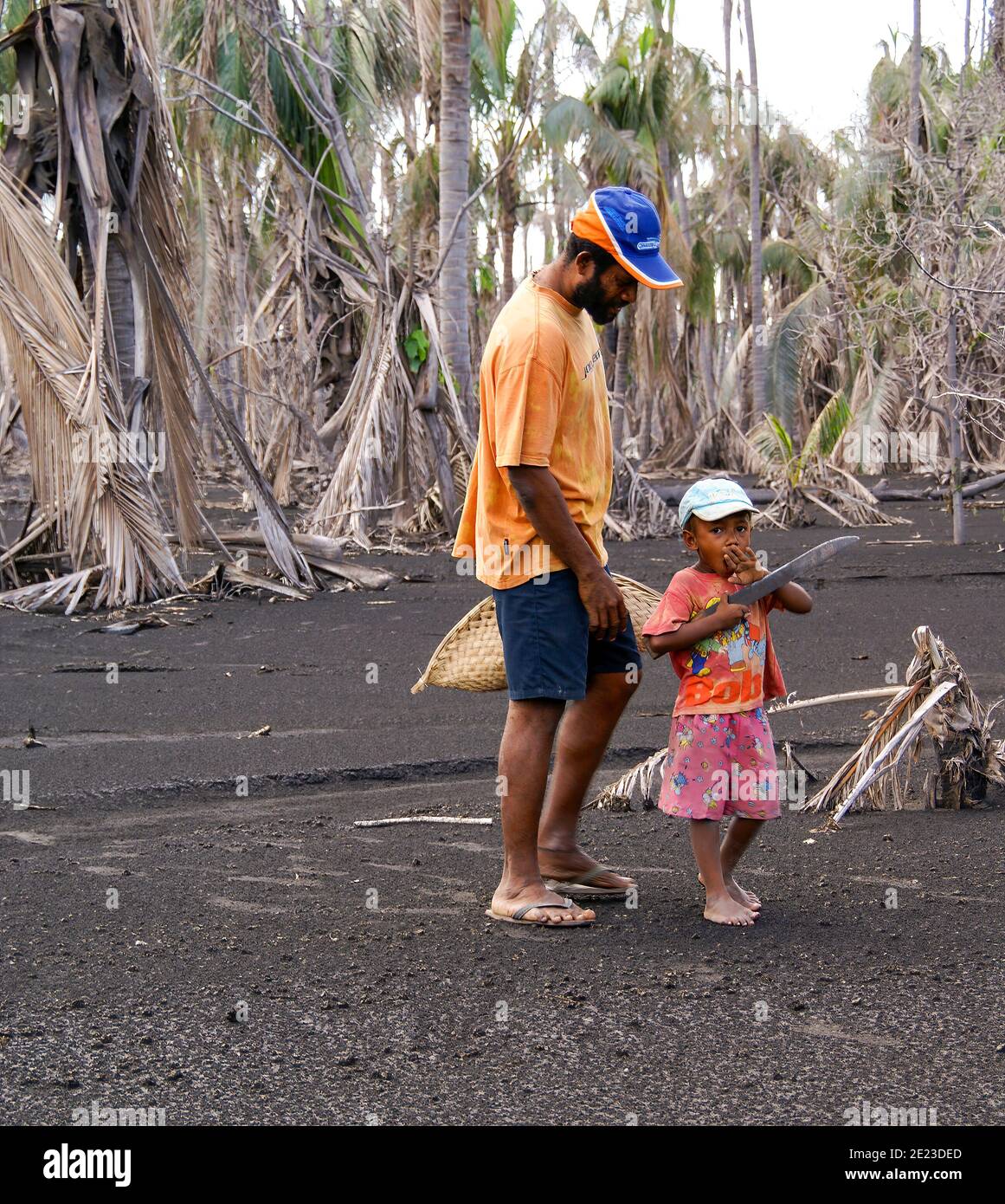 Un bambino giovane porta un grande coltello o un machete che cammina con suo padre nella sabbia nera della giungla. NMR; Rabaul; Papua Nuova Guinea Foto Stock