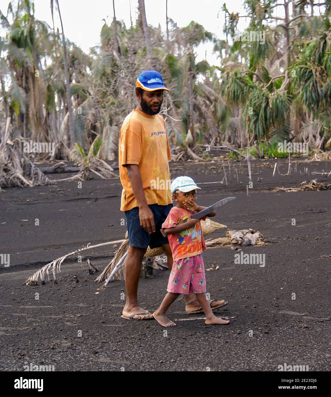 Un bambino giovane porta un grande coltello o un machete che cammina con suo padre nella sabbia nera della giungla. NMR; Rabaul; Papua Nuova Guinea Foto Stock