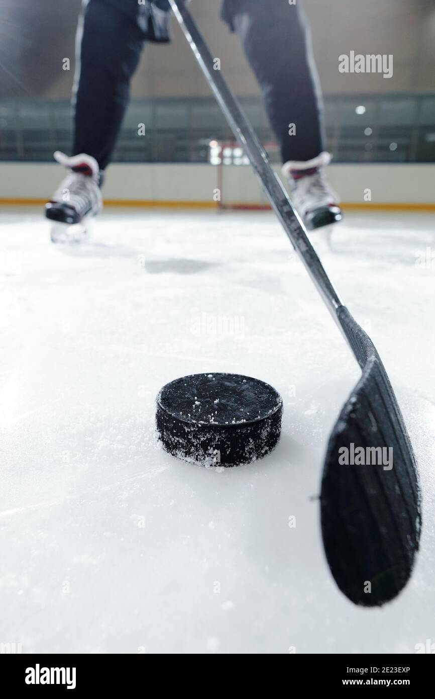 Gambe di giocatore di hockey maschile in uniforme sportiva e pattini in piedi su una pista di ghiaccio contro l'ambiente dello stadio mentre si va scatta puck Foto Stock
