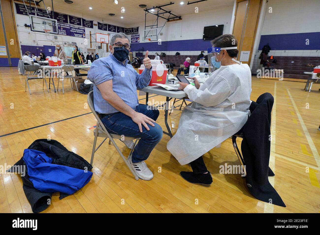 Un uomo dà a sua moglie (fuori da) un pollice-in su per una foto prima di ricevere una dose di vaccino moderno COVID-19 all'interno della Hillcrest High School, un centro designato di vaccinazione di priorità di New York City per le persone nel gruppo 1B, nel distretto di Queens di New York City, NY, 11 gennaio 2021. Il Dipartimento della Sanità ha stimato che circa 2000 persone vengono vaccinate al giorno presso la Hillcrest High School; New York City ha aperto siti di vigili del fuoco e ha in programma di aggiungerne di più per le accelerazioni della distribuzione del vaccino COVID-19, con priorità al gruppo 1B, che comprende assistenza sanitaria e lavoratori essenziali, istruzione Foto Stock