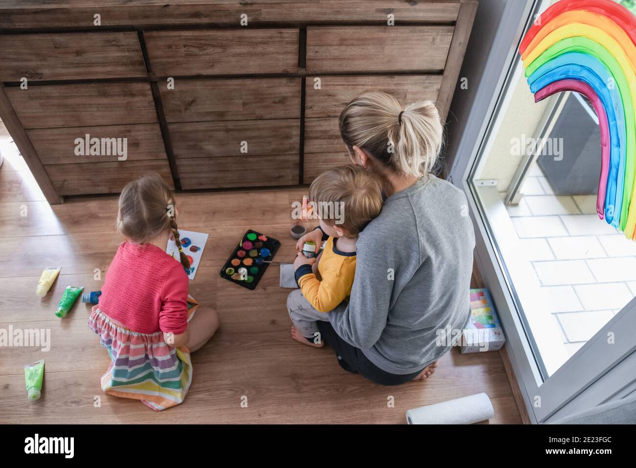 Madre e bambini dipingendo un arcobaleno sulla finestra Foto Stock