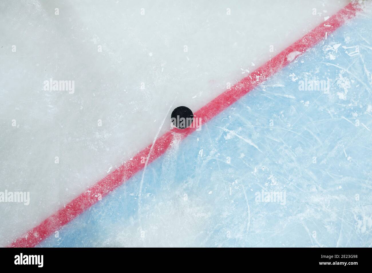 Puck giace su una linea rossa che divide lo spazio di gioco e la zona di rete su pista di ghiaccio per giocare a hockey che può essere utilizzato come sfondo Foto Stock