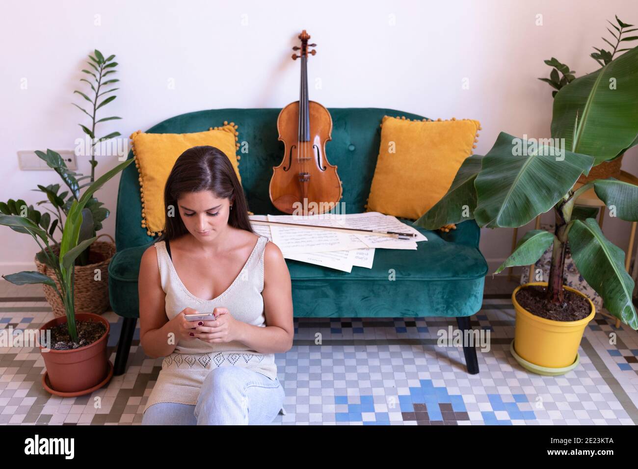 Giovane ragazza che chiacchiera sul pavimento, una viola si appoggia sul divano. Foto Stock