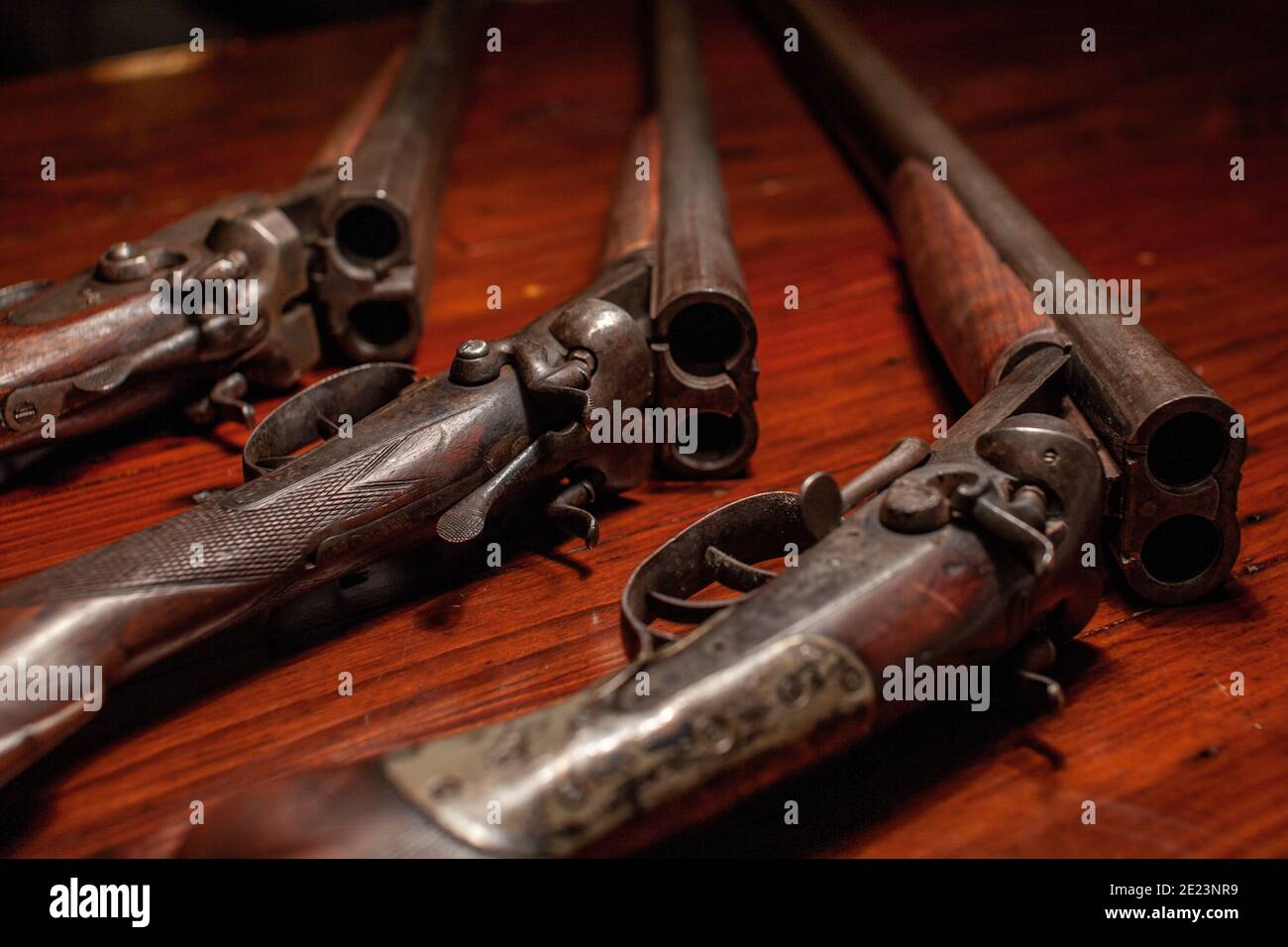 Su un tavolo di legno si trovano tre vecchi fucili a due cilindri vintage con due grilletti e due martelli. Il loro bluing si è sbiadito ad una patina. Foto Stock