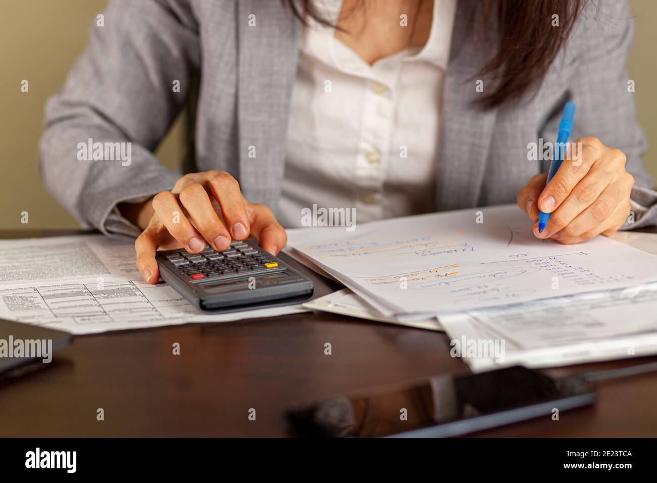 Una donna d'affari che indossa un abito formale sta lavorando in un ambiente d'ufficio. Sta calcolando i redditi e le spese usando le dichiarazioni, le polizze di paga, le ricevute. S Foto Stock