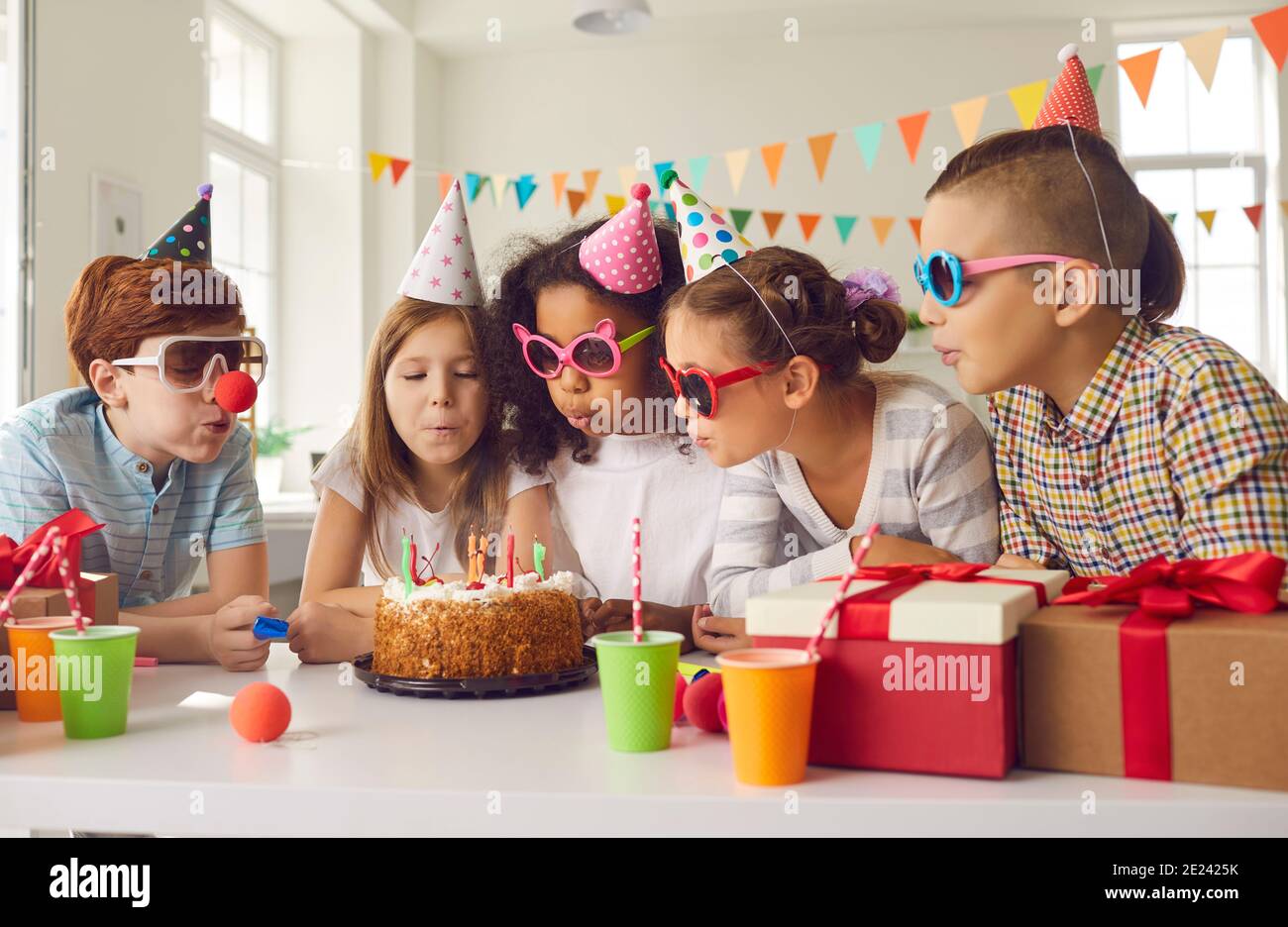 Gruppo di bambini tutti insieme che soffia candele su torta di compleanno a festa di divertimento a casa Foto Stock