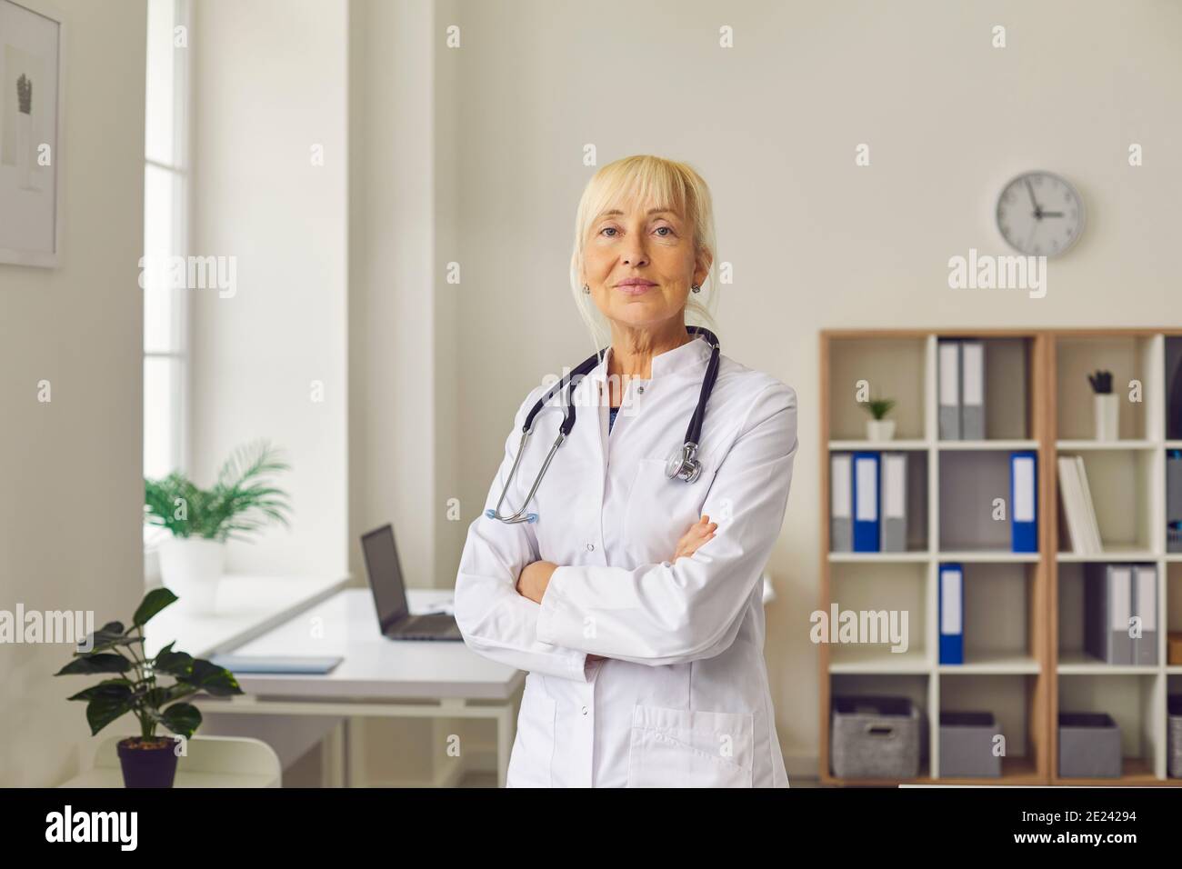 Positivo sicuro anziano donna medico in piedi e guardare uniforme alla telecamera Foto Stock