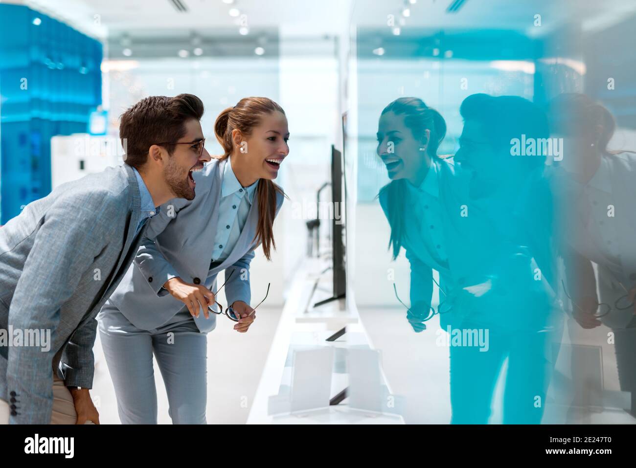 Multiculturale felice coppia vestito in abiti da lavoro alla ricerca di nuovo televisore da acquistare. Interni del negozio di tecnologia. Foto Stock