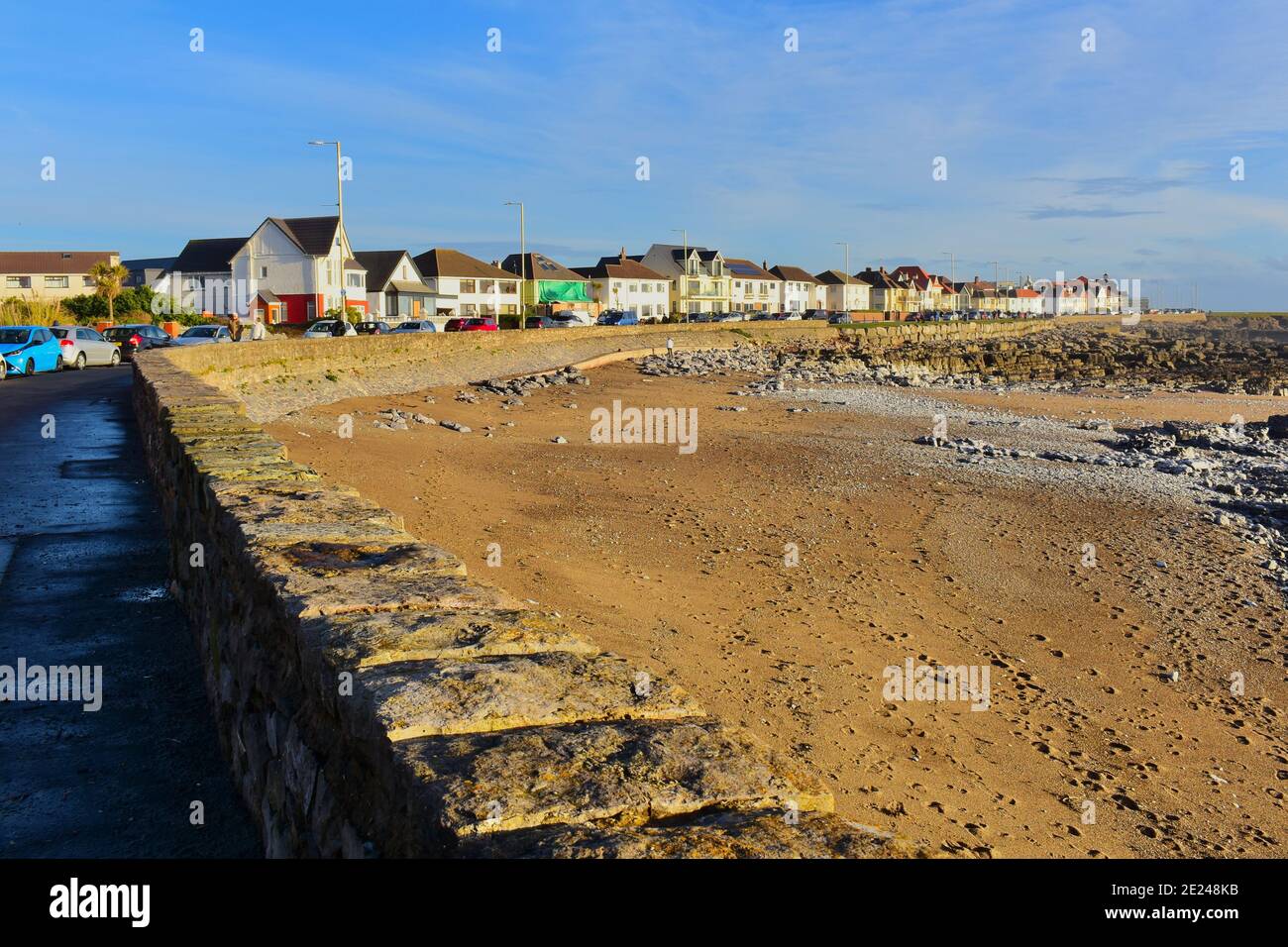 La passeggiata a Porthcarwl con case che si affacciano sul mare. A bassa marea si rivela la costa rocciosa con solo una piccola area di sabbia. Foto Stock