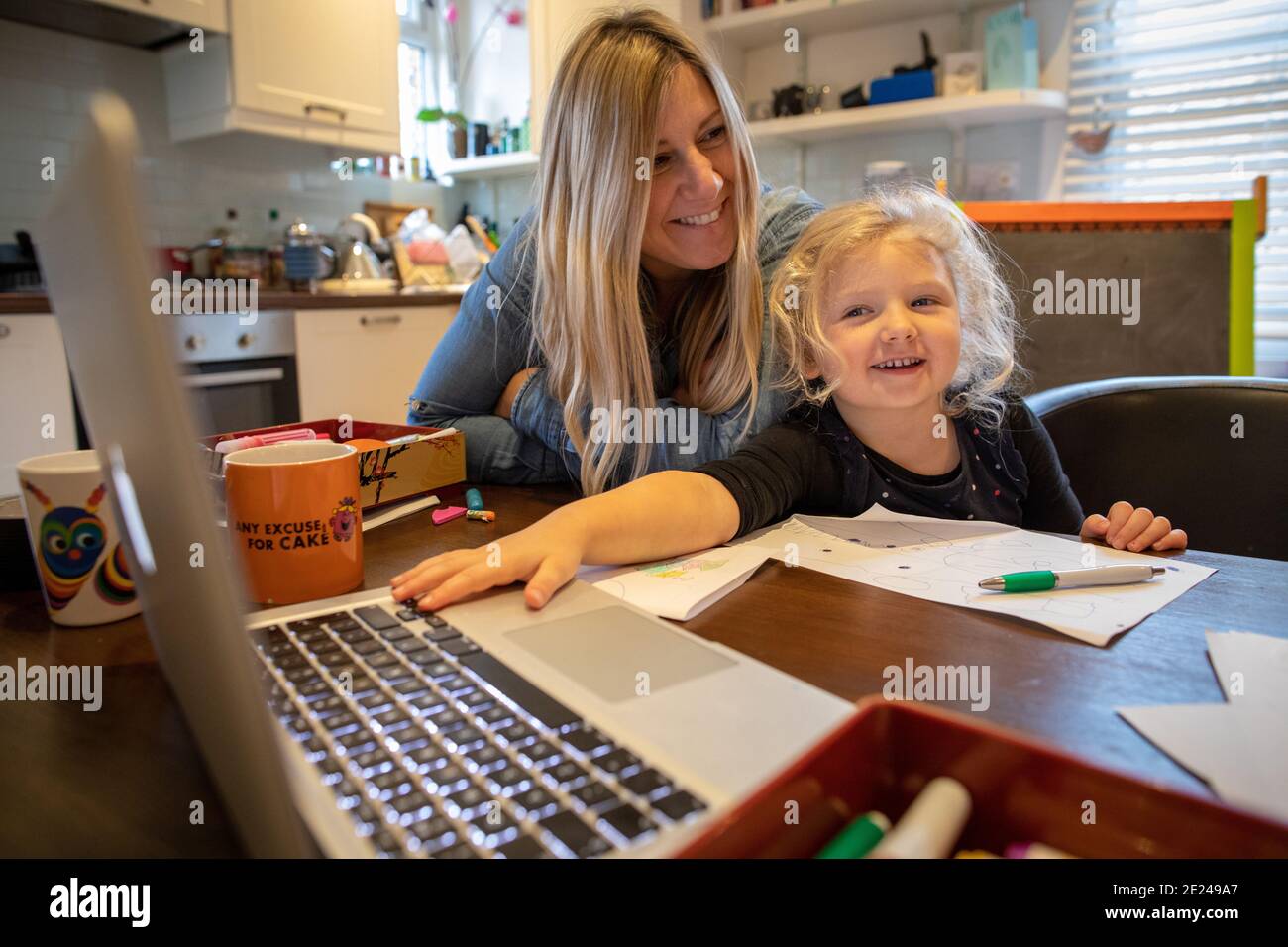Una bambina di tre anni che impara a casa con la mamma utilizzando un computer portatile sul tavolo da cucina. Foto Stock