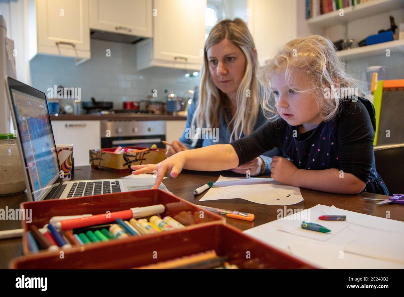 Una bambina di tre anni che impara a casa con la mamma utilizzando un computer portatile sul tavolo da cucina. Foto Stock