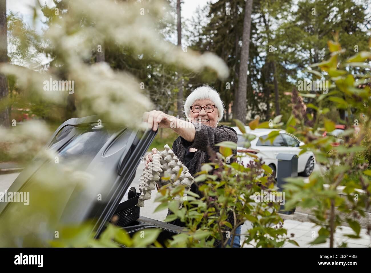 Donna anziana sorridente che mette i rifiuti in bidone Foto Stock