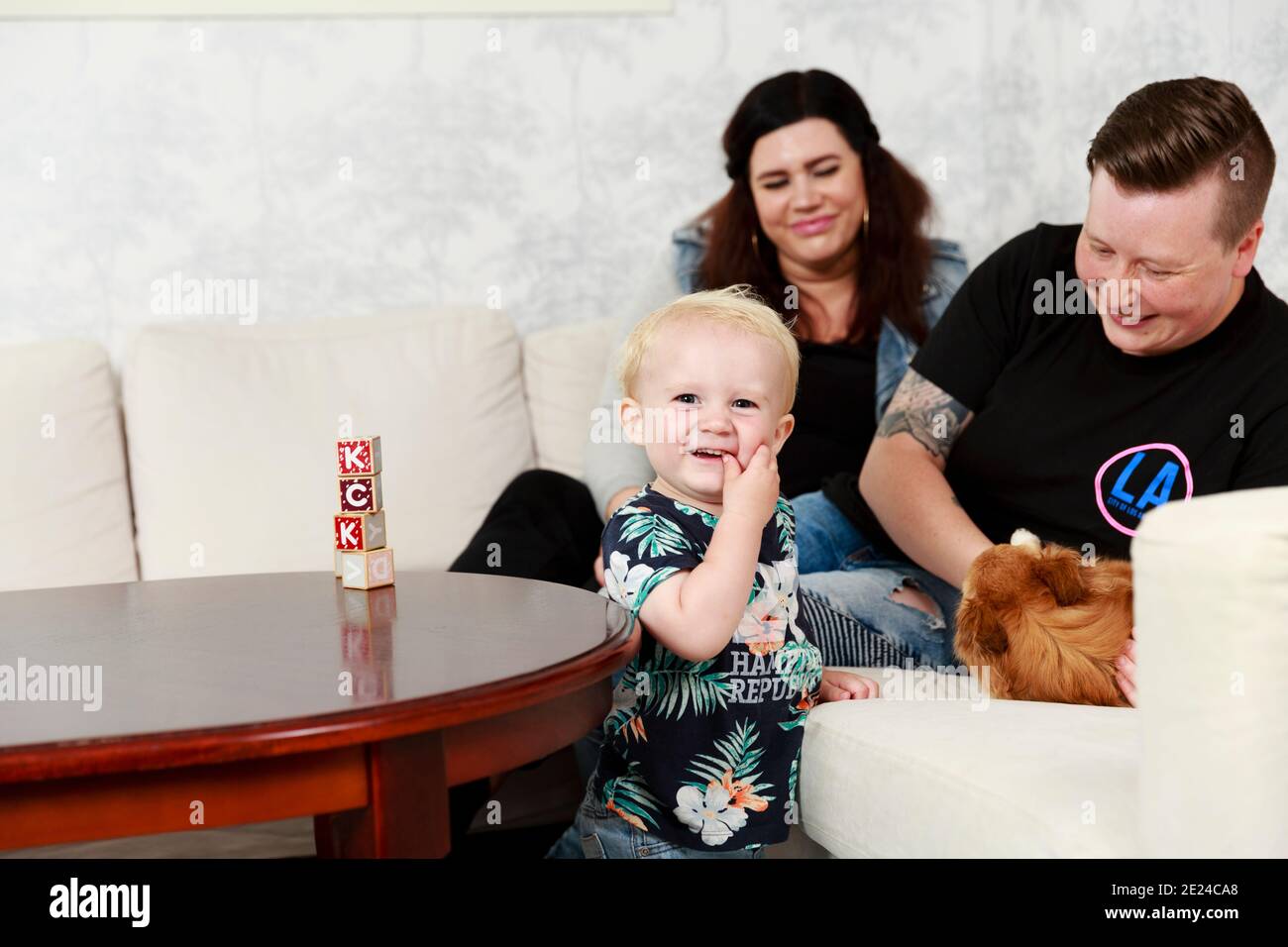 Bambino sorridente in soggiorno, madri sullo sfondo Foto Stock