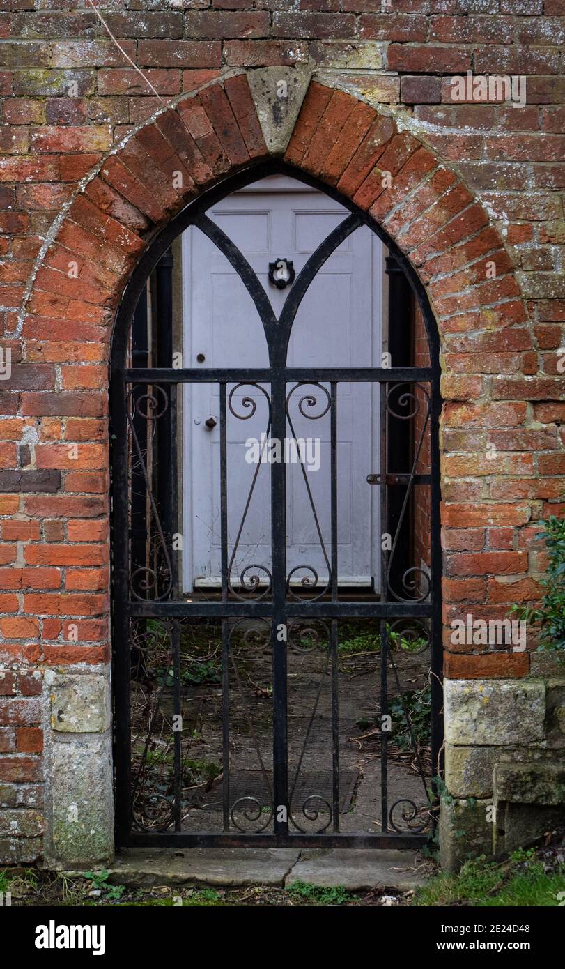 Arco in mattoni contenente ferro battuto, cancello ad arco a Church Street, Westbury, Wiltshire, UK, che si affaccia su All Saints Church. Foto Stock