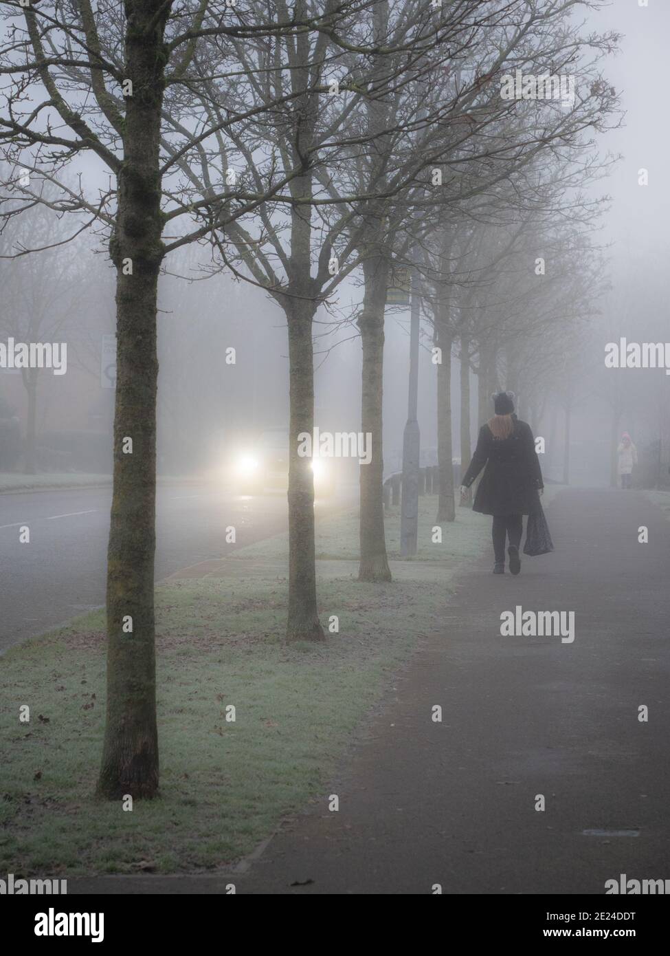 Le donne pedoni camminano in una mattinata nebbiosa mentre una macchina passa con i fari accesi. Nel Wiltshire, Inghilterra, Regno Unito. Foto Stock
