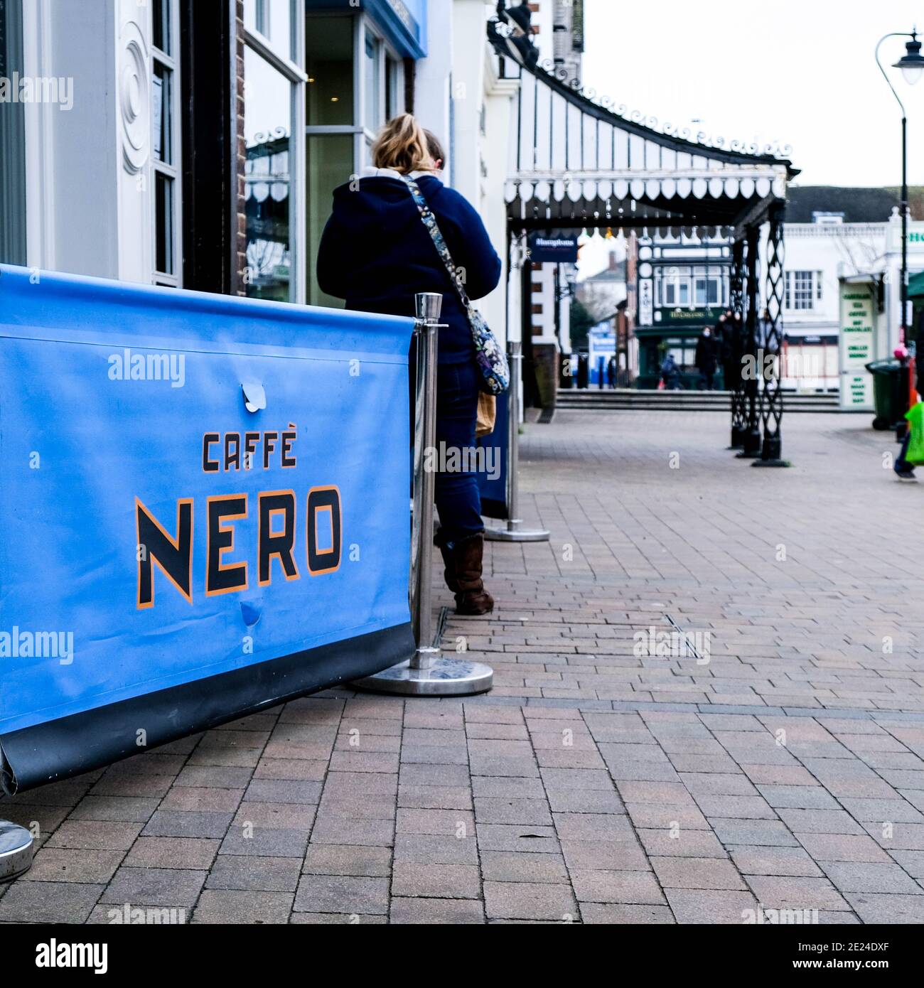Londra UK, Donna in piedi da solo fuori UN caffè Nero Cafe Coffee Shop su e vuoto High Street durante Covid-19 Pandemic Lockdown Foto Stock