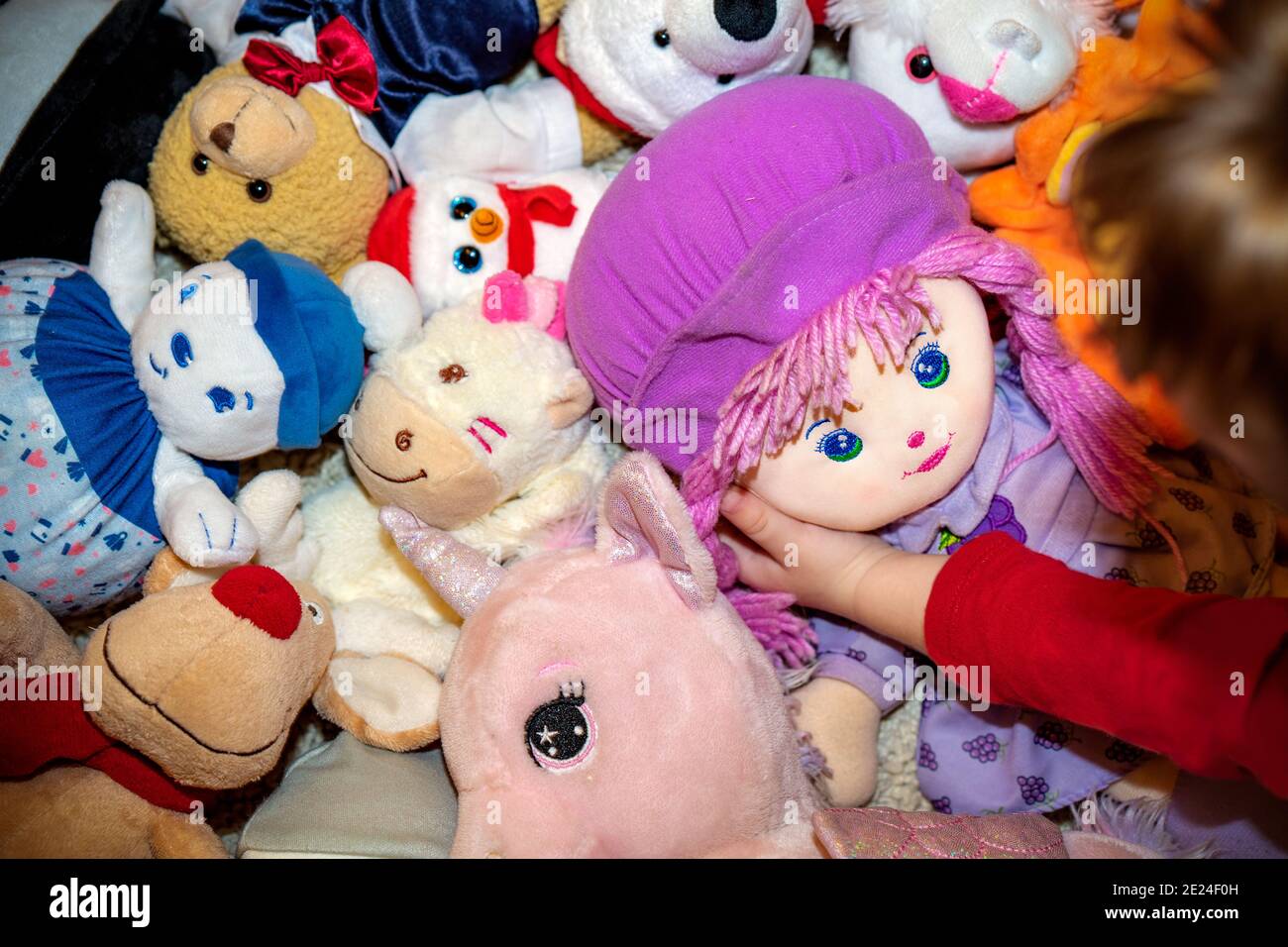 diversi tipi di peluche morbidi giocattoli sul pavimento ovunque nella stanza di un bambino con un gilrl che gioca con lei la bambola preferita Foto Stock