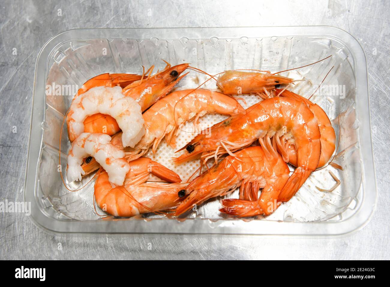 Cotti gamberetti freschi interi in un contenitore di plastica con due code sgusciate in cima in un concetto di gourmet ingredienti di pesce per cucinare o un Foto Stock