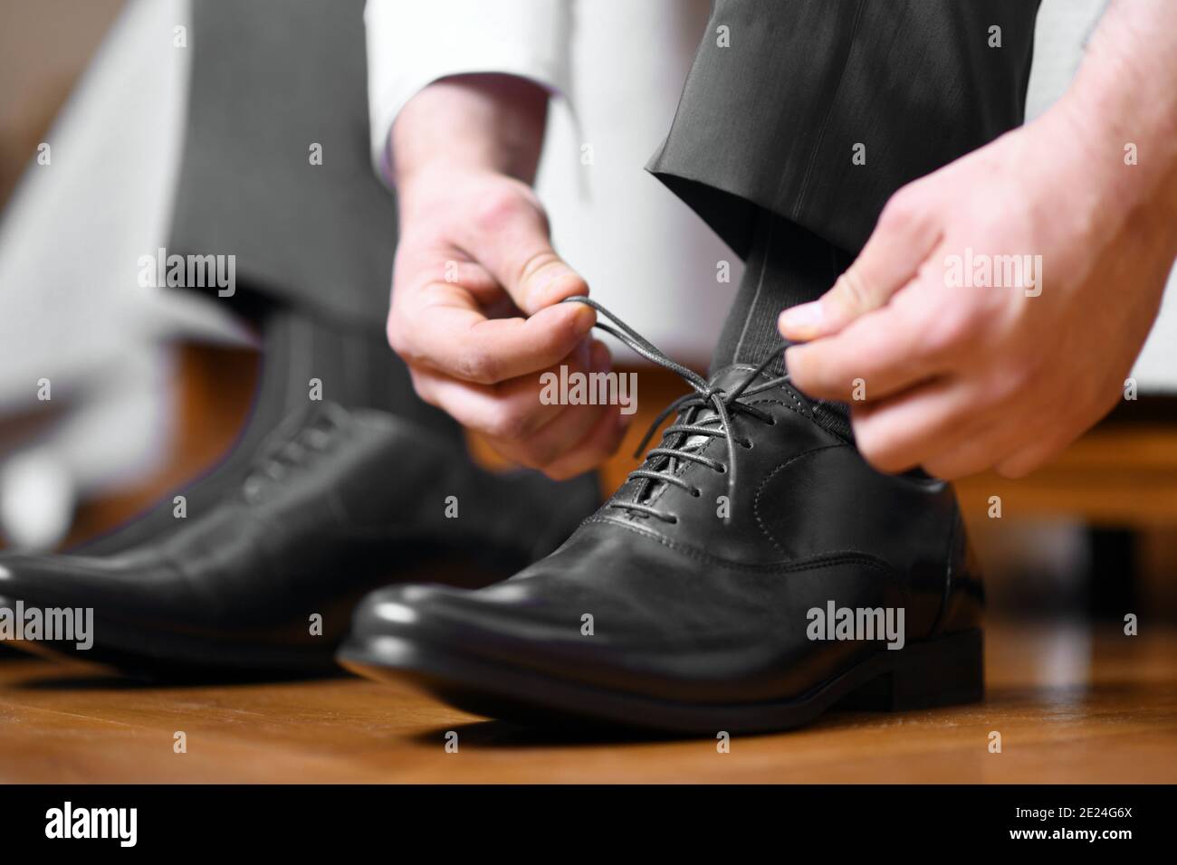 Uomo d'affari legando scarpe su scarpe classiche eleganti nere in pelle, o sposo vestirsi in preparazione per il giorno del matrimonio. Primo piano da un lato Foto Stock