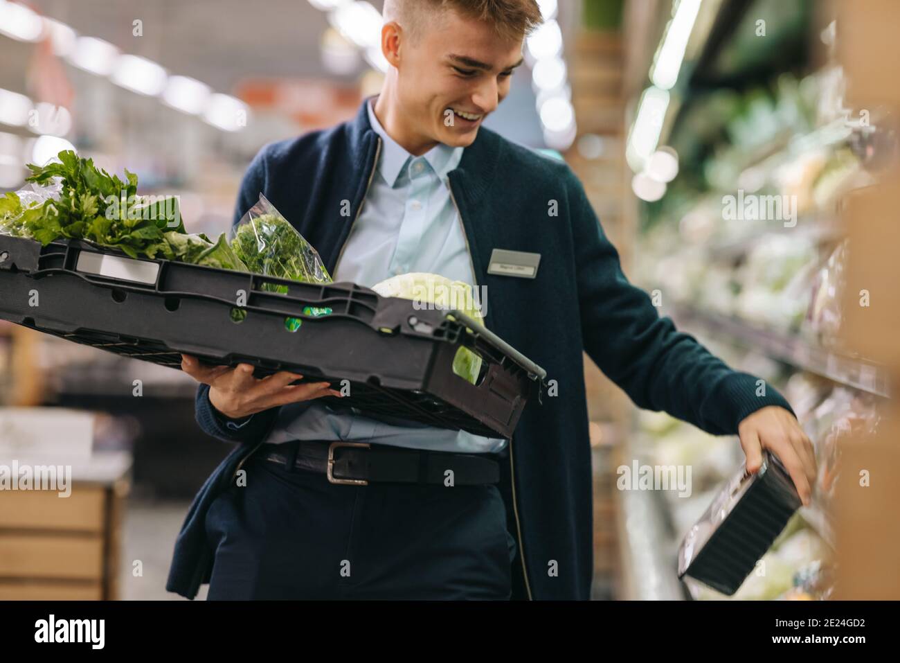 Uomo che lavora nella sezione di produzione di un supermercato. Uomo che rifornisce il rack con prodotti freschi. Foto Stock