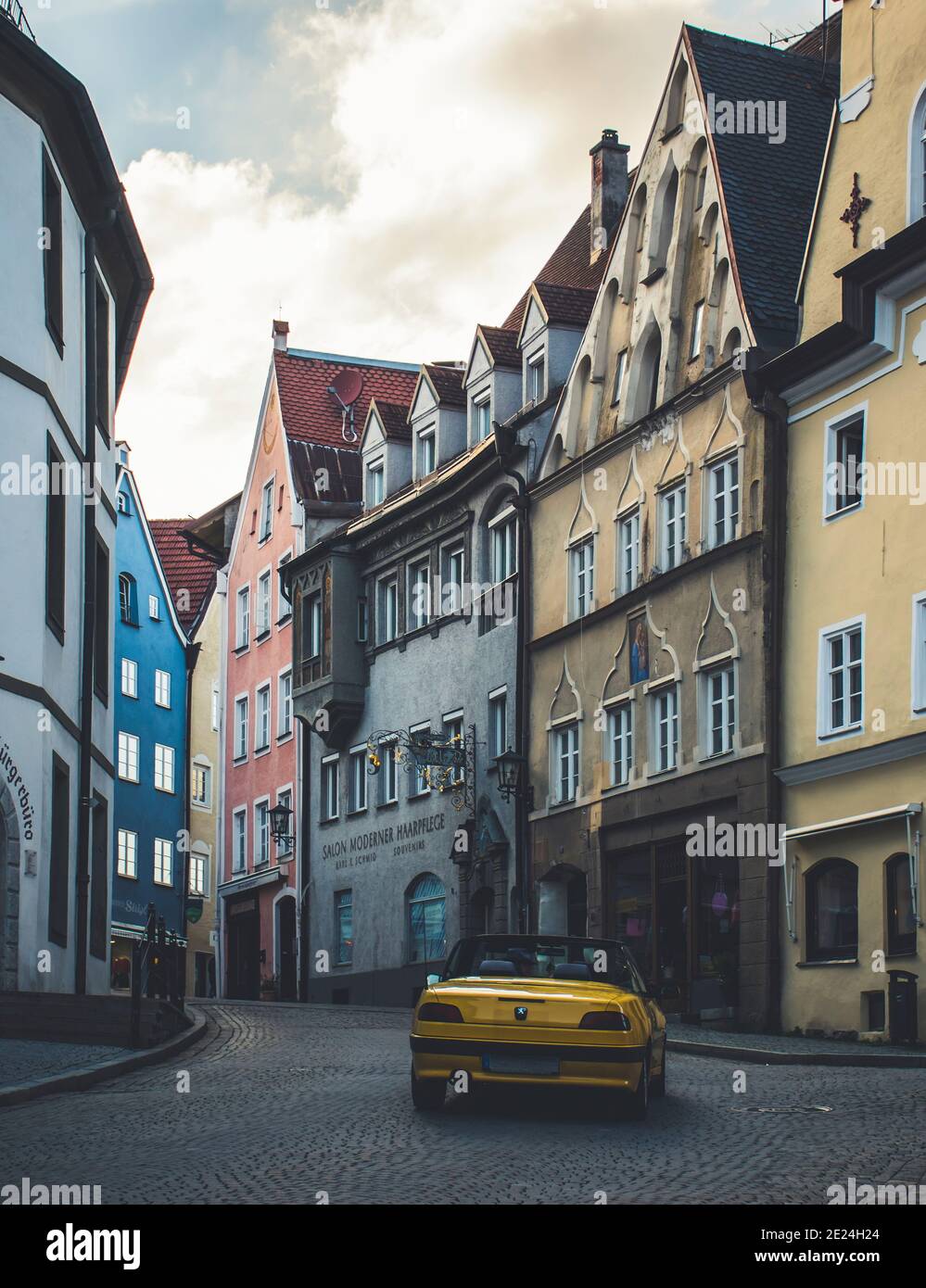 Füssen, Germania 26 maggio 2019 - Coppia felice di guidare in auto cabriolet gialla sopra la vecchia romantica città europea senza persone. Foto Stock