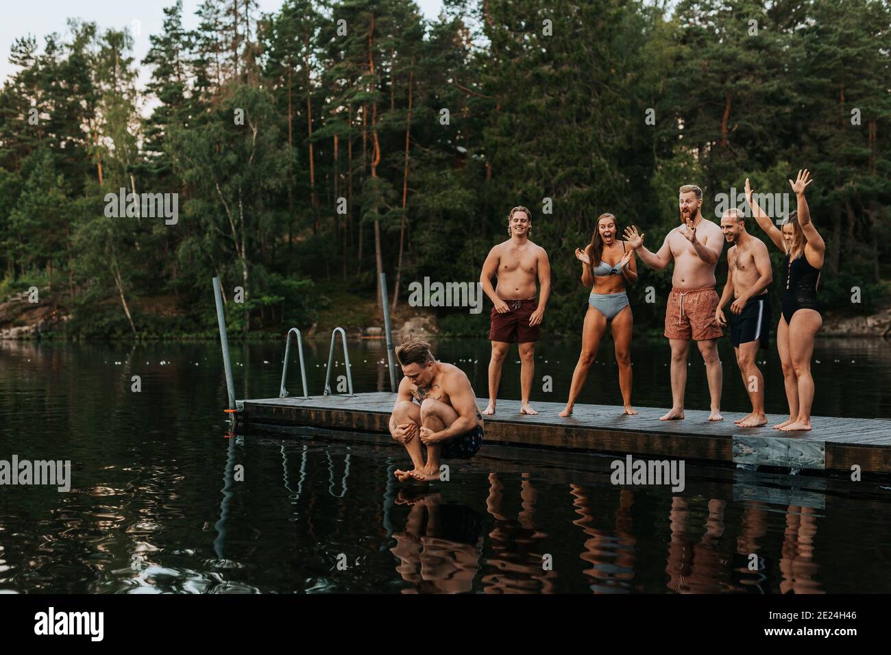 Amici che si acclamano quando l'uomo salta in acqua Foto Stock