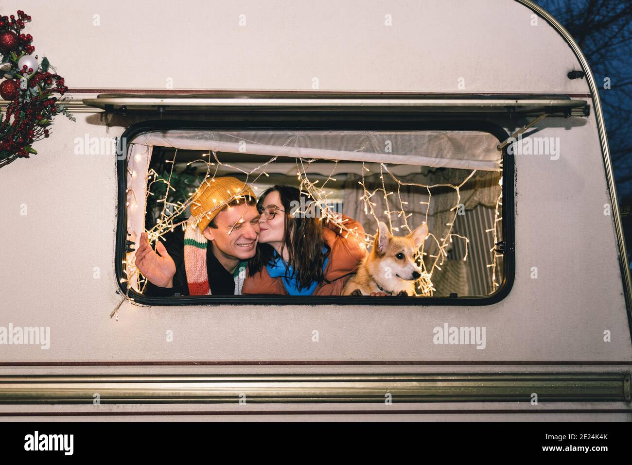 Felice coppia caucasica con cane di corgi in caravan o campervan. Donna che baciava un uomo, vestiti invernali casual, corda leggera Foto Stock