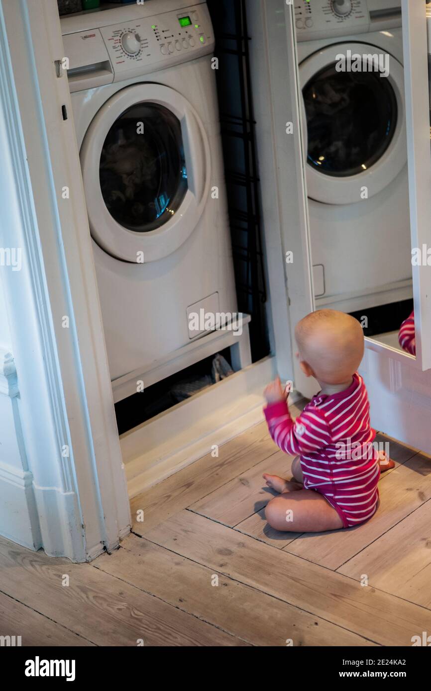 Bambina seduta di fronte alla lavatrice Foto Stock