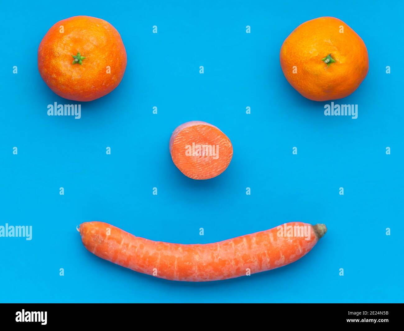 Una divertente composizione di mandarini e carote nella forma di un volto sorridente su uno sfondo azzurro Foto Stock