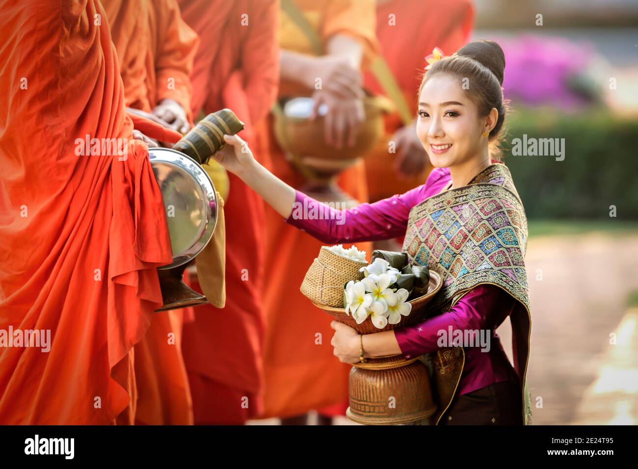 Donna inginocchiata davanti a tre monaci che offrono elemosine, Thailandia Foto Stock