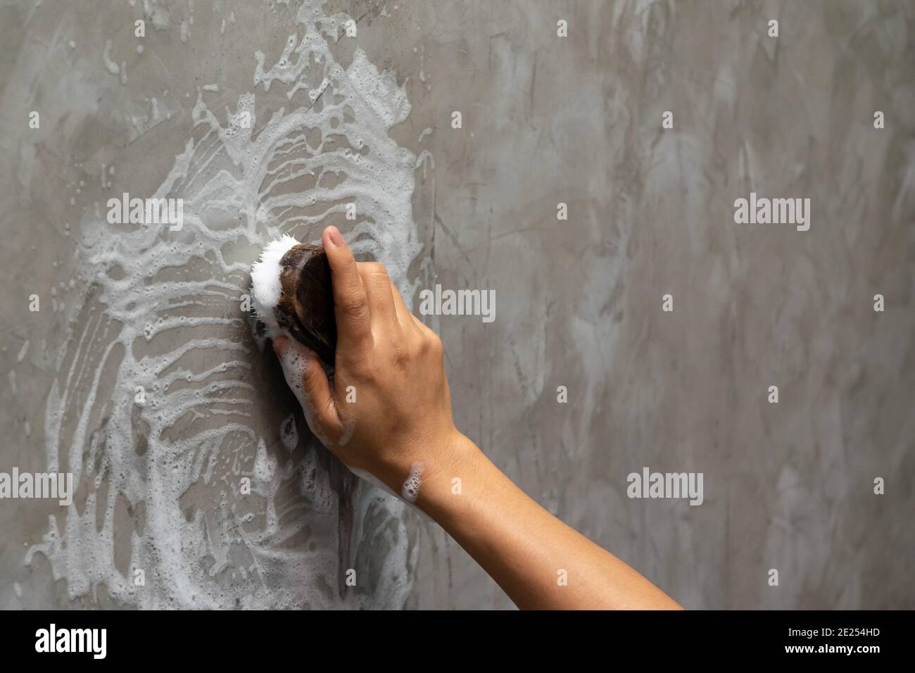 Mano della donna usata per convertire la pulizia di lucidatura sulla parete di calcestruzzo. Foto Stock