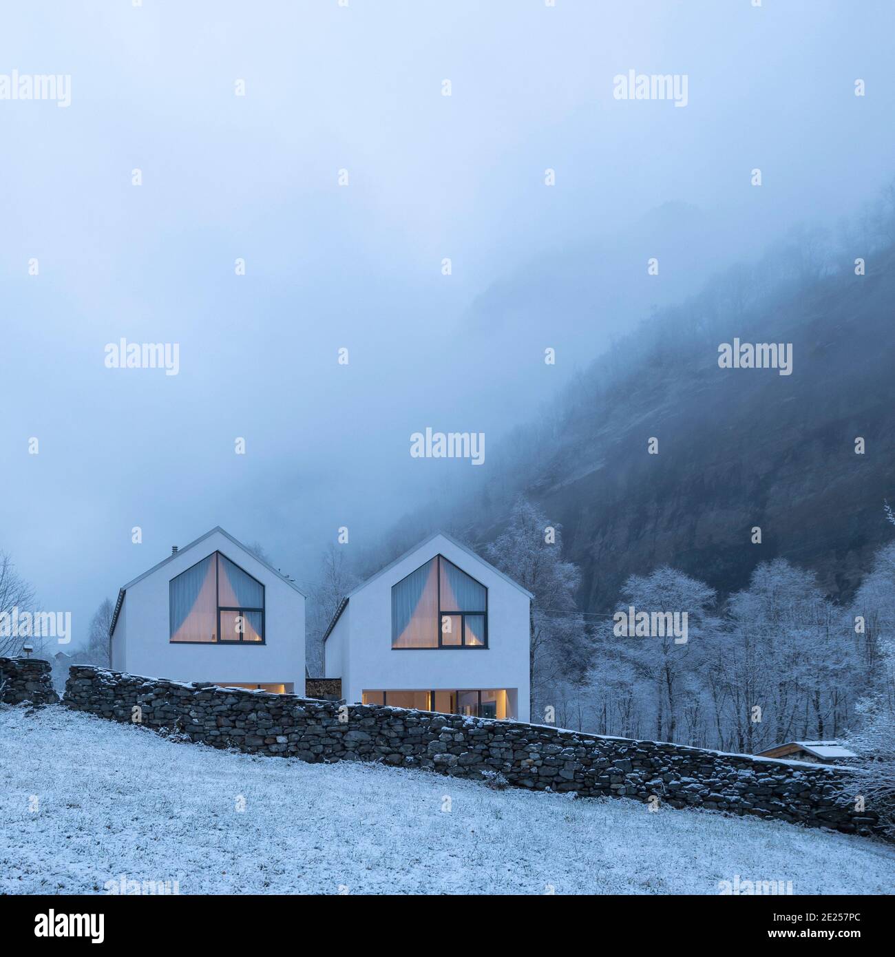 Moderna casa bianca con grandi finestre sorrondate dalla natura, neve e nebbia. Umore di Chirstmas. Nessuno dentro. Foto Stock