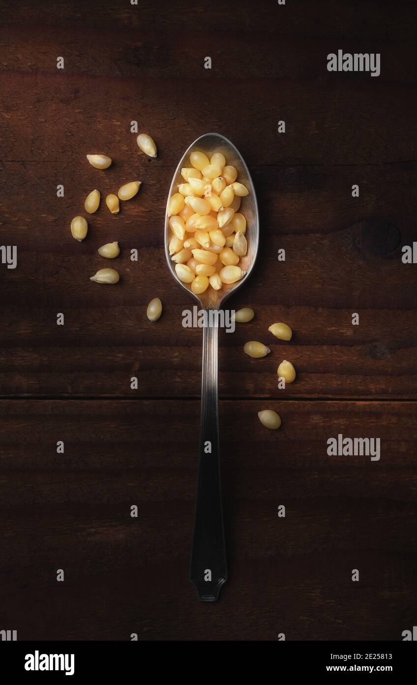 Cucchiaio di popcorn pieno di noccioli su un rustico tavolo di legno scuro. Verticale con luce laterale calda e spazio per la copia. Foto Stock