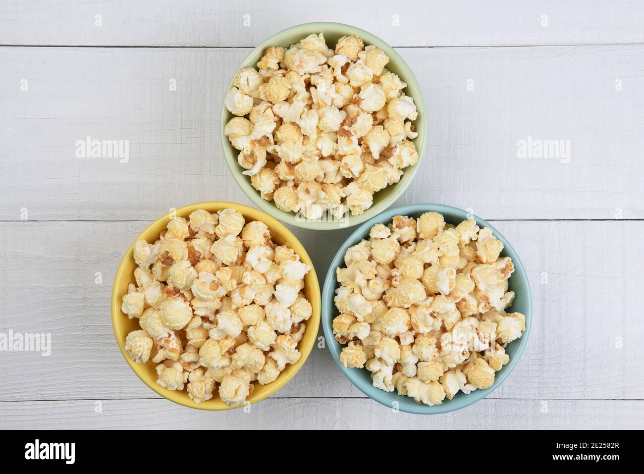 Colpo di testa di tre diverse ciotole colorate riempite di popcorn fresco, su un tavolo di legno bianco. Foto Stock