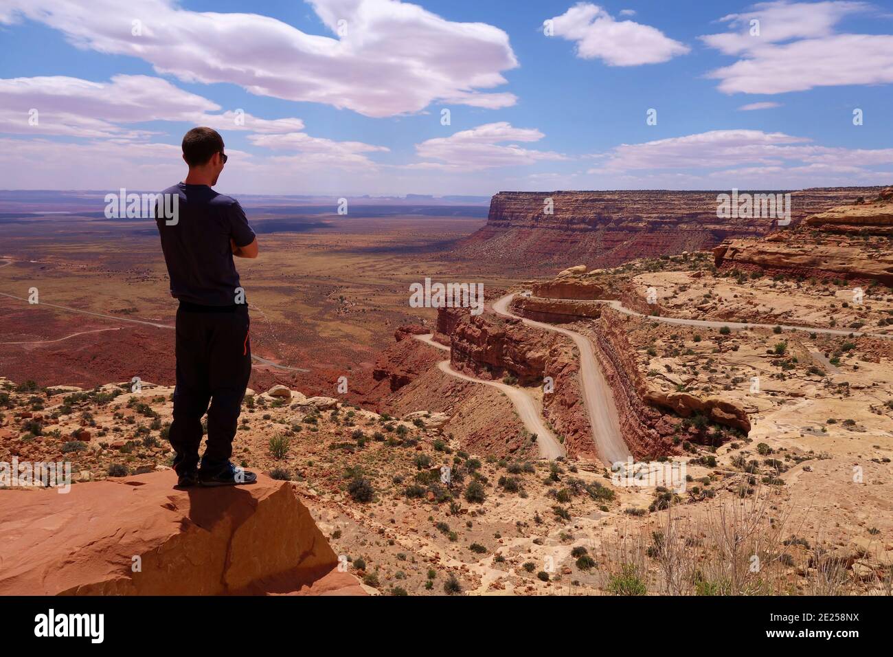 Giovane uomo che domina la scena spettacolare del canyon nello Utah/Arizona, nel deserto sud-occidentale degli Stati Uniti, con cielo blu brillante e nuvole soffici. Foto Stock