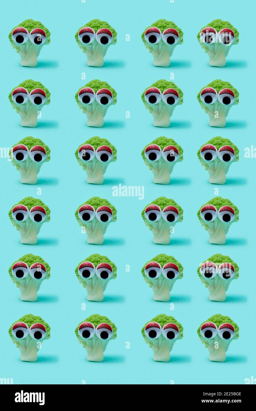 alcune teste di broccoli con gli occhi d'oca divertenti che si levano in piedi su un sfondo blu Foto Stock