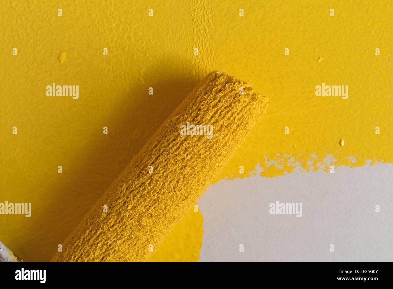 Utilizzando un piccolo rullo, verniciare la vernice gialla su una superficie illuminata da luce del finestrino. Foto Stock