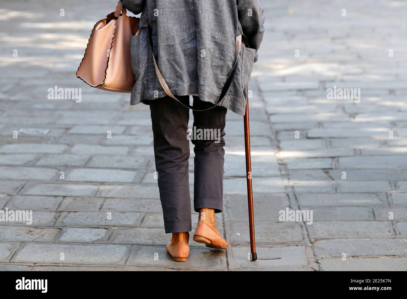 Una vecchia donna con un bastone che cammina per strada. Foto Stock