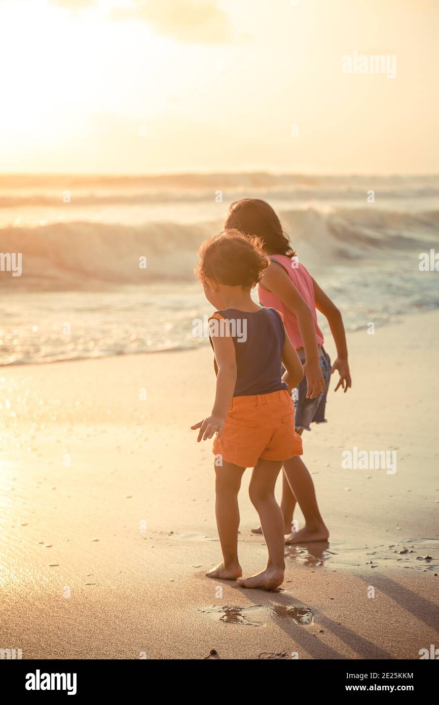 bambini etnici asiatici che esplorano la riva del mare al tramonto Foto Stock