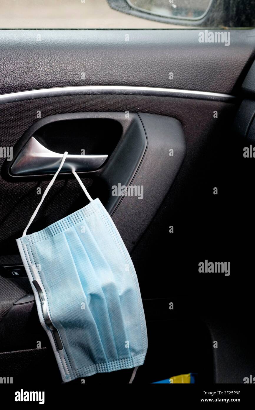 Una maschera monouso appesa alla maniglia di una porta dell'auto durante la pandemia di Covid-19. Foto Stock