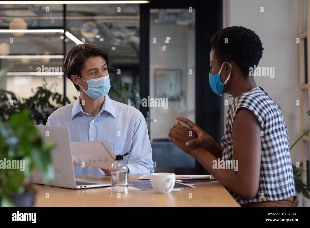 Diverse persone di affari che indossano maschere di fronte seduti utilizzando il laptop andare attraverso la documentazione in ufficio Foto Stock